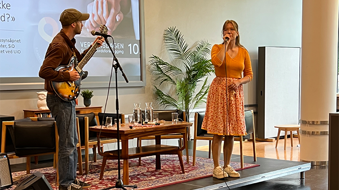 Man på gitar og kvinne med mikrofon på en scene. 
