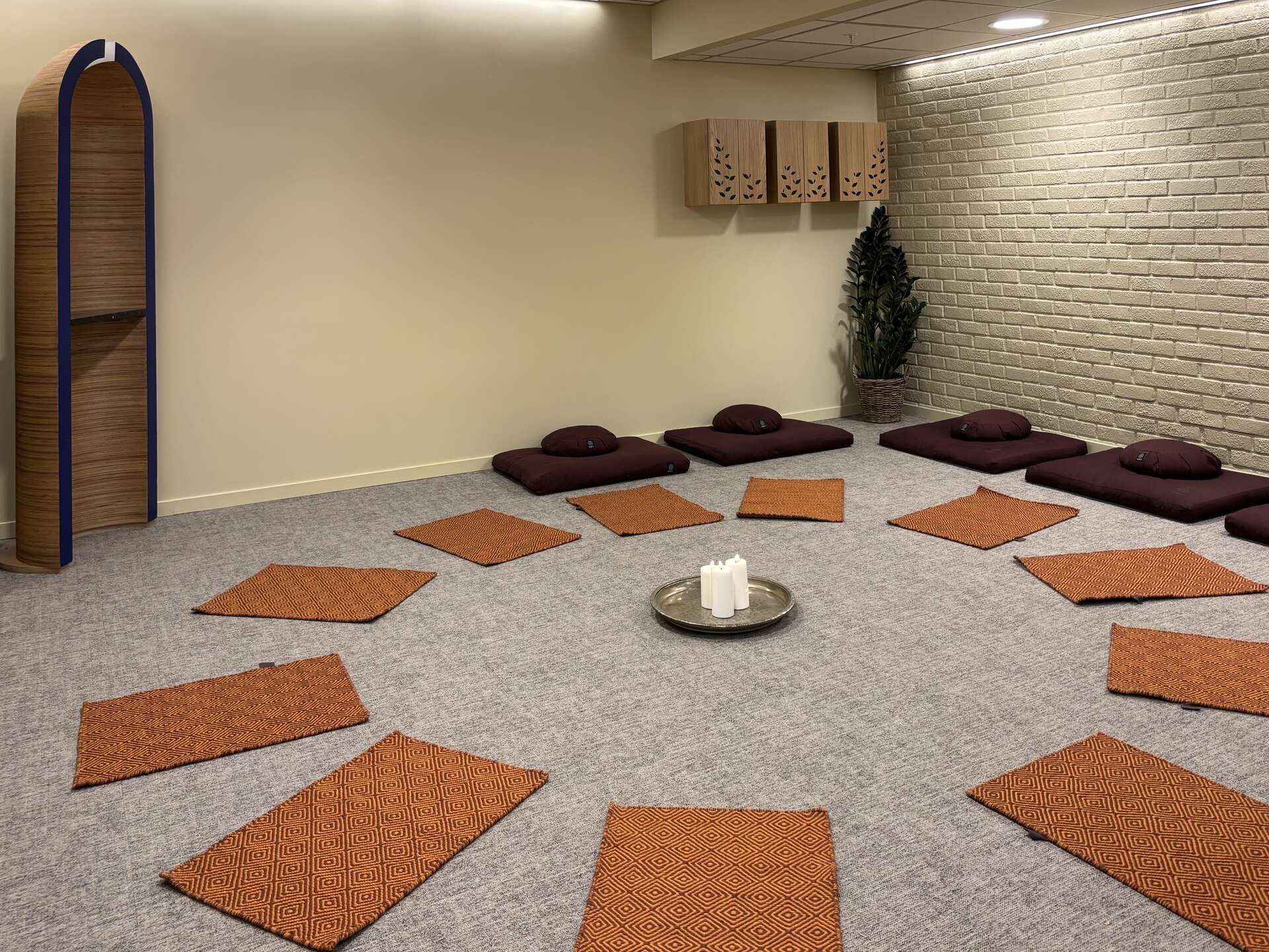 Bilde av et rom med bønnetepper lagt ut i sirkel, med milrab i hjørnet og meditasjonsplasser langs veggen. 